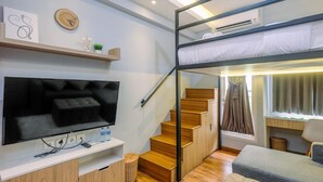 A modern hotel room with a bunk bed, a flat-screen TV, a desk, and a staircase. - Enjoy and New Furnished Studio at Podomoro Golf View Apartment (Gunung Putri)