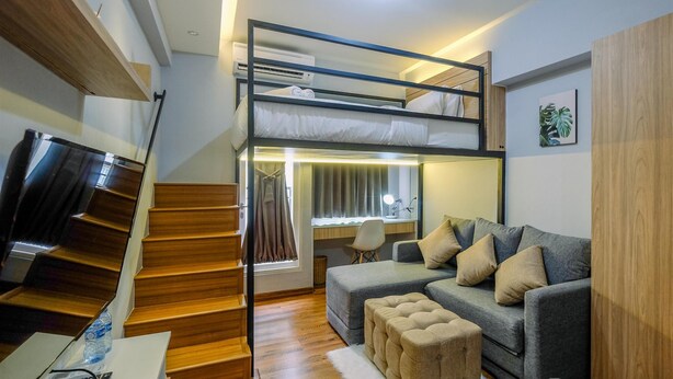 A modern room with a bunk bed, a desk with a chair, a grey sofa, and a staircase. - Enjoy and New Furnished Studio at Podomoro Golf View Apartment (Gunung Putri)