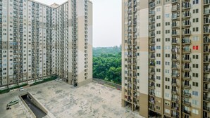 A high-rise residential building with multiple balconies, a parking area, and a view of a green landscape. - Simply Design 2BR at Podomoro Golf View Apartment (Gunung Putri)