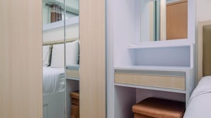 A compact hotel room with a bed, a bedside table, a mirror, and a small seating area with a cushioned bench. - Simply Design 2BR at Podomoro Golf View Apartment (Gunung Putri)