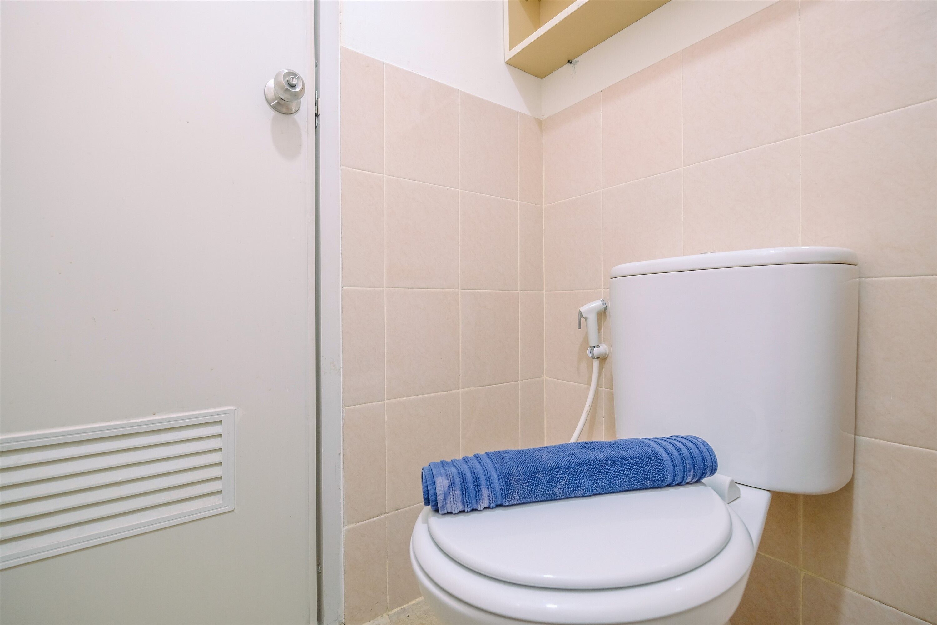A bathroom with a toilet, beige tiles, and a blue towel on the seat.
