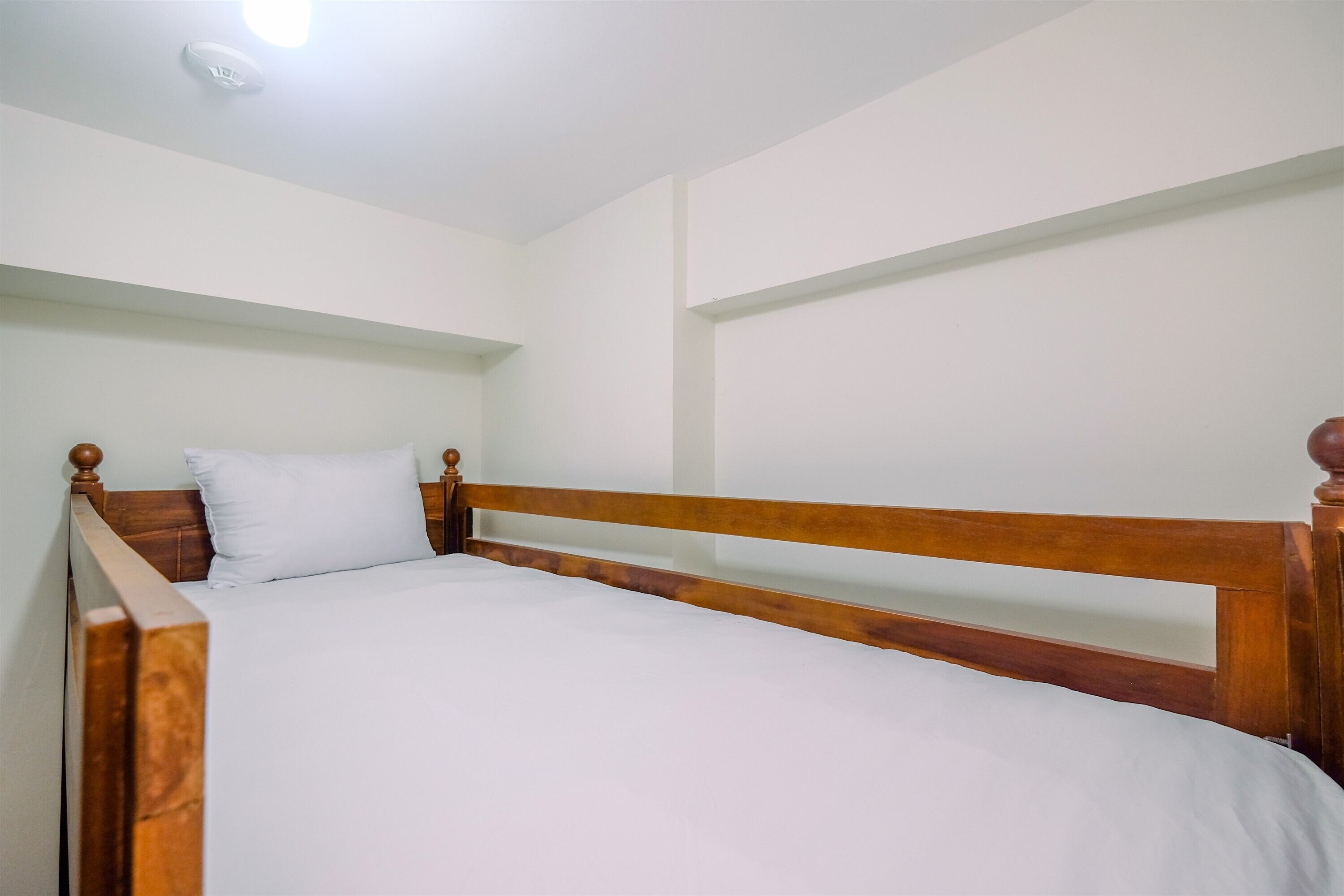 A single bed with wooden headboard and footboard, white bedding, and a ceiling light fixture.