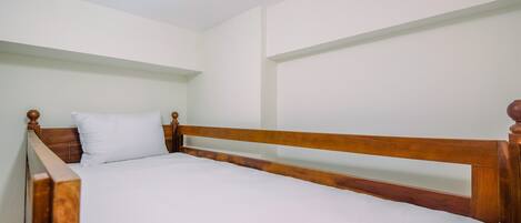 Una cama individual con cabecera y piecera de madera, ropa de cama blanca y una lámpara en el techo.