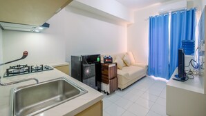 A compact living space with a kitchenette, a sofa, a TV, and a curtain. - Nice and Comfort 2BR at Podomoro Golf View Apartment (Gunung Putri)
