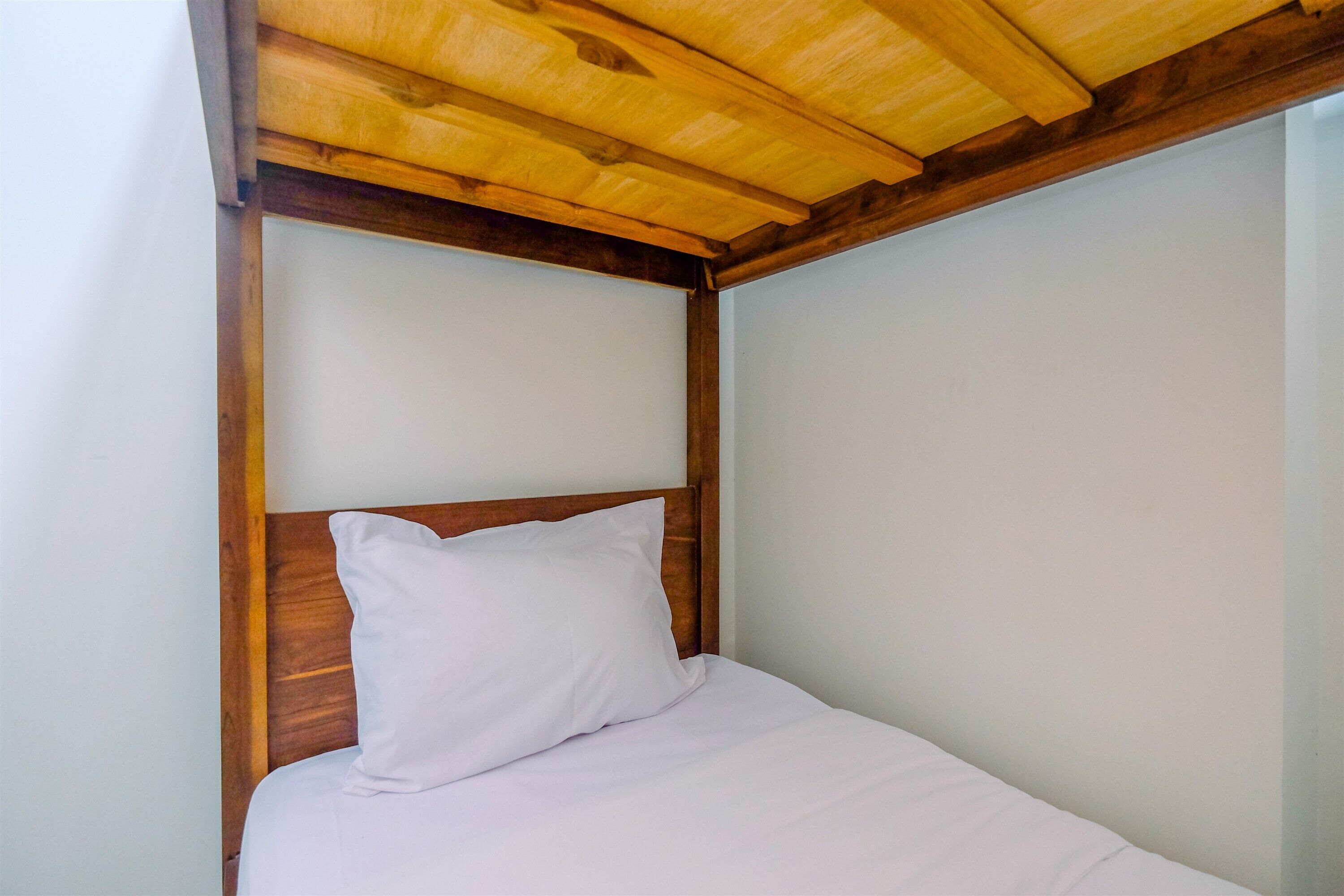 A single bed with a wooden headboard and white bedding in a room with white walls.