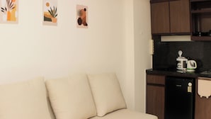A kitchenette with a black dishwasher, a coffee maker, and a microwave. There is a beige sofa with two cushions. - Nice and Comfort 1BR with Extra Room at Podomoro Golf View Apartment (Gunung Putri)
