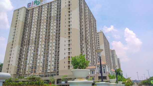A high-rise residential building with multiple balconies, a PGV logo, and a well-maintained garden area with planters. - Nice and Comfort 1BR with Extra Room at Podomoro Golf View Apartment (Gunung Putri)