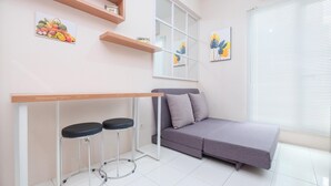 Un espace de vie moderne avec un canapé gris, deux tabourets de bar, une table en bois et des œuvres d’art accrochées aux murs.