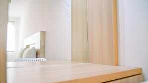 A minimalist room with a wooden bed frame, a white wall, and a large mirror. - Dashing Studio at Baileys Apartment (South Tangerang)