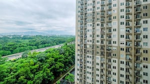 A high-rise building with multiple balconies and a view of a green landscape with trees and a road. - Comfort Podomoro Golf View 2BR Apartment (Gunung Putri)