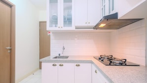 A kitchen with white cabinets, a granite countertop, a gas stove, and a stainless steel sink. - Comfort Podomoro Golf View 2BR Apartment (Gunung Putri)
