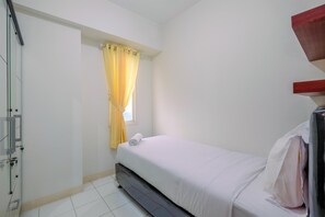 Una habitación pequeña con cama individual, ventana, cortina y cama con colchón y almohada blancos.