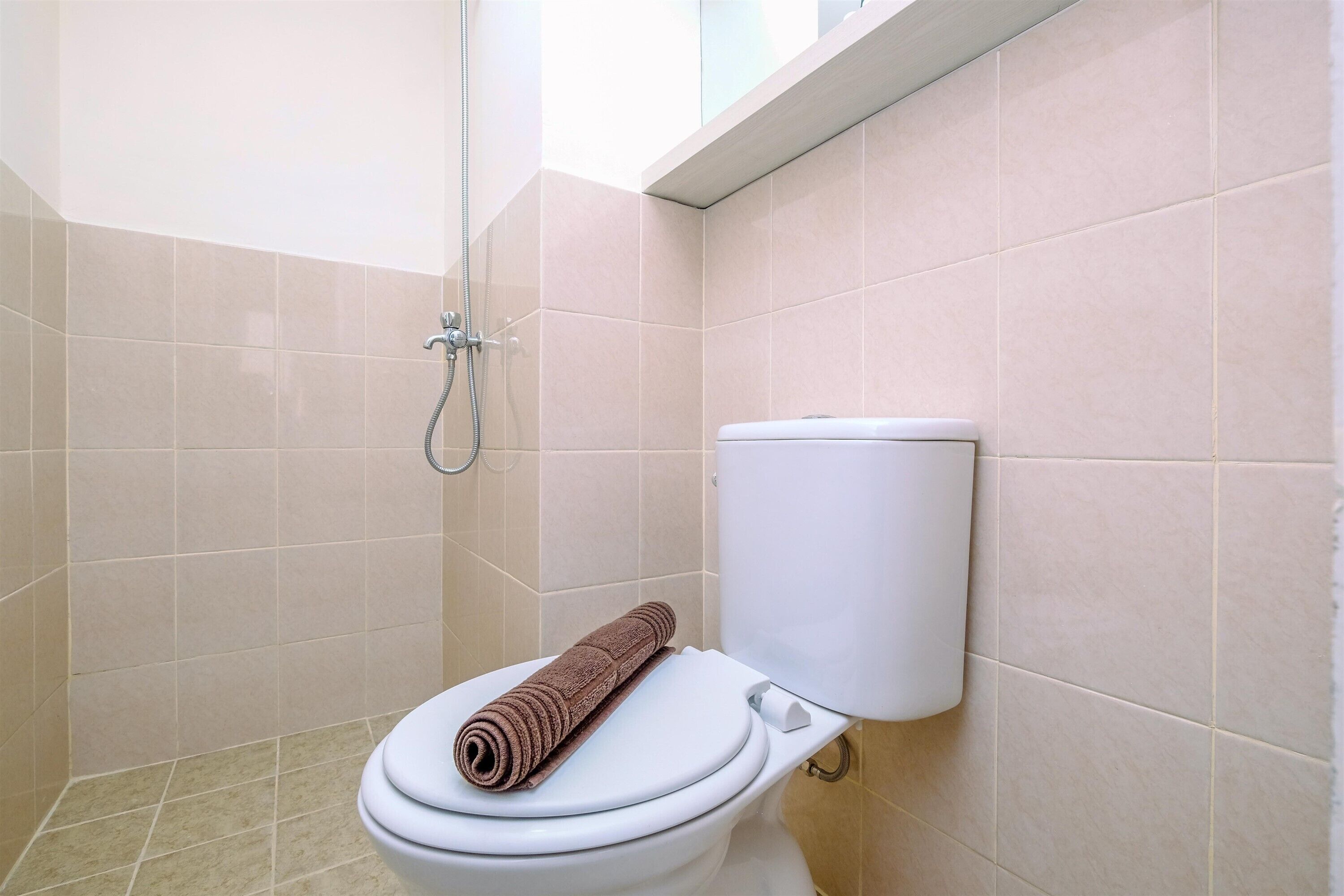 Egy fürdőszoba, amelyben WC, zuhanyzó és bézs színű csempével borított falak találhatók.