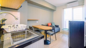 A modern kitchen with a built-in stove, a sink with a dish rack, and a dining area with a table and chairs. - Minimalist and Warm 2BR at 29th Floor Podomoro Golf View Apartment (Gunung Putri)