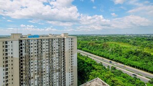 A high-rise building with multiple floors and balconies, overlooking a highway and lush greenery. - Minimalist and Warm 2BR at 29th Floor Podomoro Golf View Apartment (Gunung Putri)