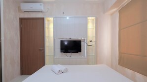 A hotel room with a bed, a television mounted on the wall, a door, and an air conditioning unit. - Comfort and Stylish 2BR at Podomoro Golf View Apartment (Gunung Putri)