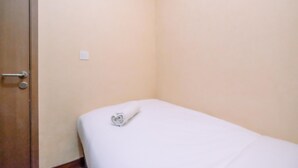 Une petite chambre avec un lit simple, une porte en bois et un matelas blanc.