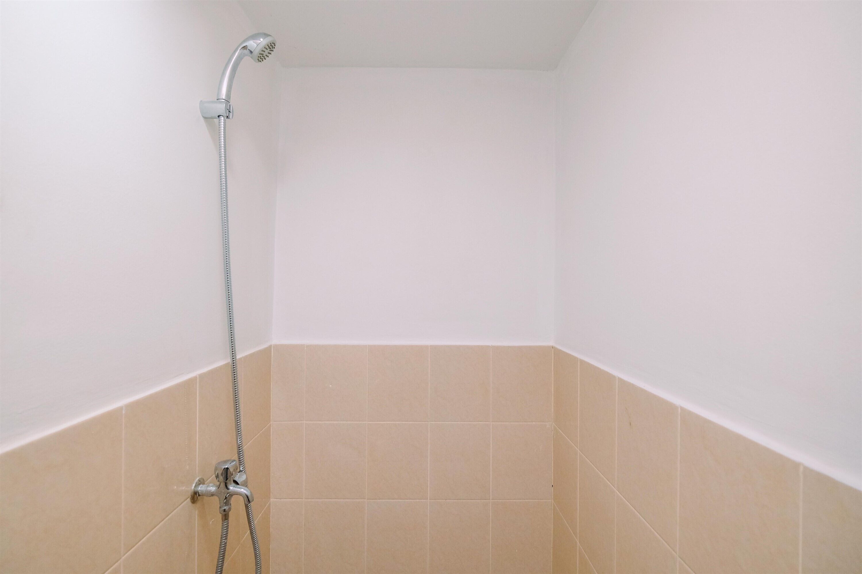 A corner of a bathroom with a shower head and hose, beige tiles, and white walls.