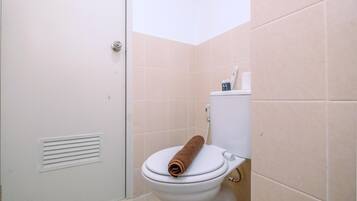 Une salle de bain avec des toilettes blanches, des carreaux beiges et une serviette posée sur le siège.