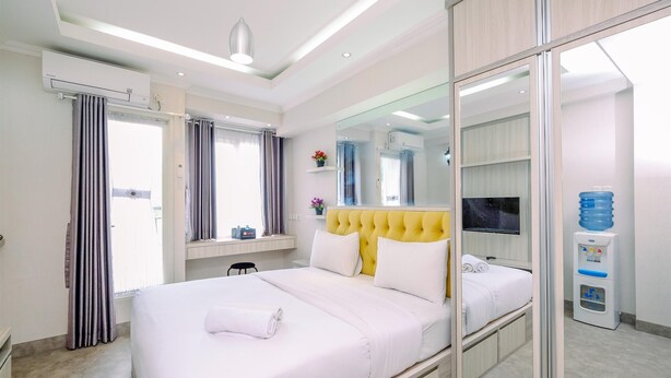 A hotel room with a large bed, a TV, a water dispenser, and a mirror. - Homey Studio Room at Podomoro Golf View Apartment (Gunung Putri)