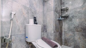 A modern bathroom with a toilet, a shower, and marble tiles. - Homey Studio Room at Podomoro Golf View Apartment (Gunung Putri)