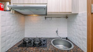 A compact kitchen with a gas stove, stainless steel sink, and a modern range hood. - Homey Studio Room at Podomoro Golf View Apartment (Gunung Putri)