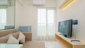 Una sala de estar moderna con un sofá color beige, una mesa de centro de vidrio, un televisor de pantalla plana sobre un soporte de madera y un equipo de aire acondicionado en la pared.