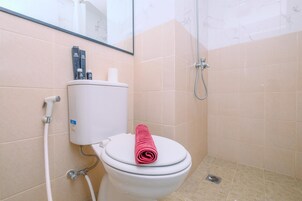 Um banheiro com vaso sanitário, chuveiro e suporte para papel higiênico.