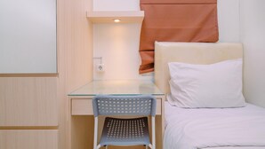 Una habitación compacta con un escritorio de vidrio, una silla individual, una cama con almohada blanca y una cortina marrón.