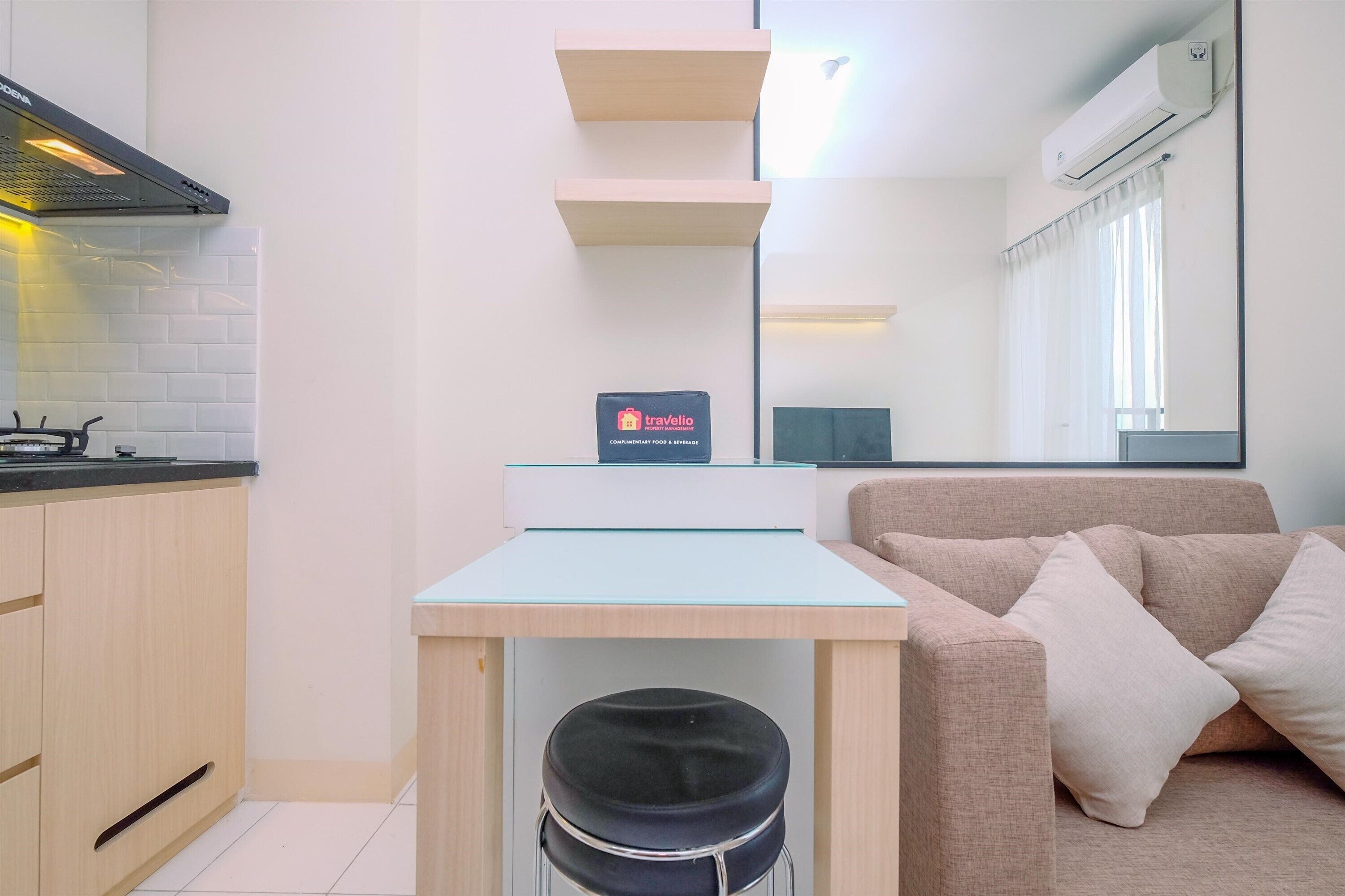 A modern kitchen with a gas stove, a small table, and a sofa. There is a sign on the table and an air conditioning unit on the wall.
