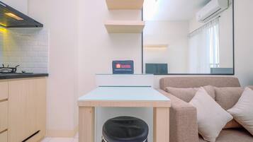 A modern kitchen with a gas stove, a small table, and a sofa. There is a sign on the table and an air conditioning unit on the wall.
