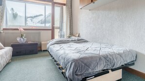 Ein Schlafzimmer mit Bett, Schminktisch, Fenster mit Blick auf eine verschneite Landschaft und Heizkörper.