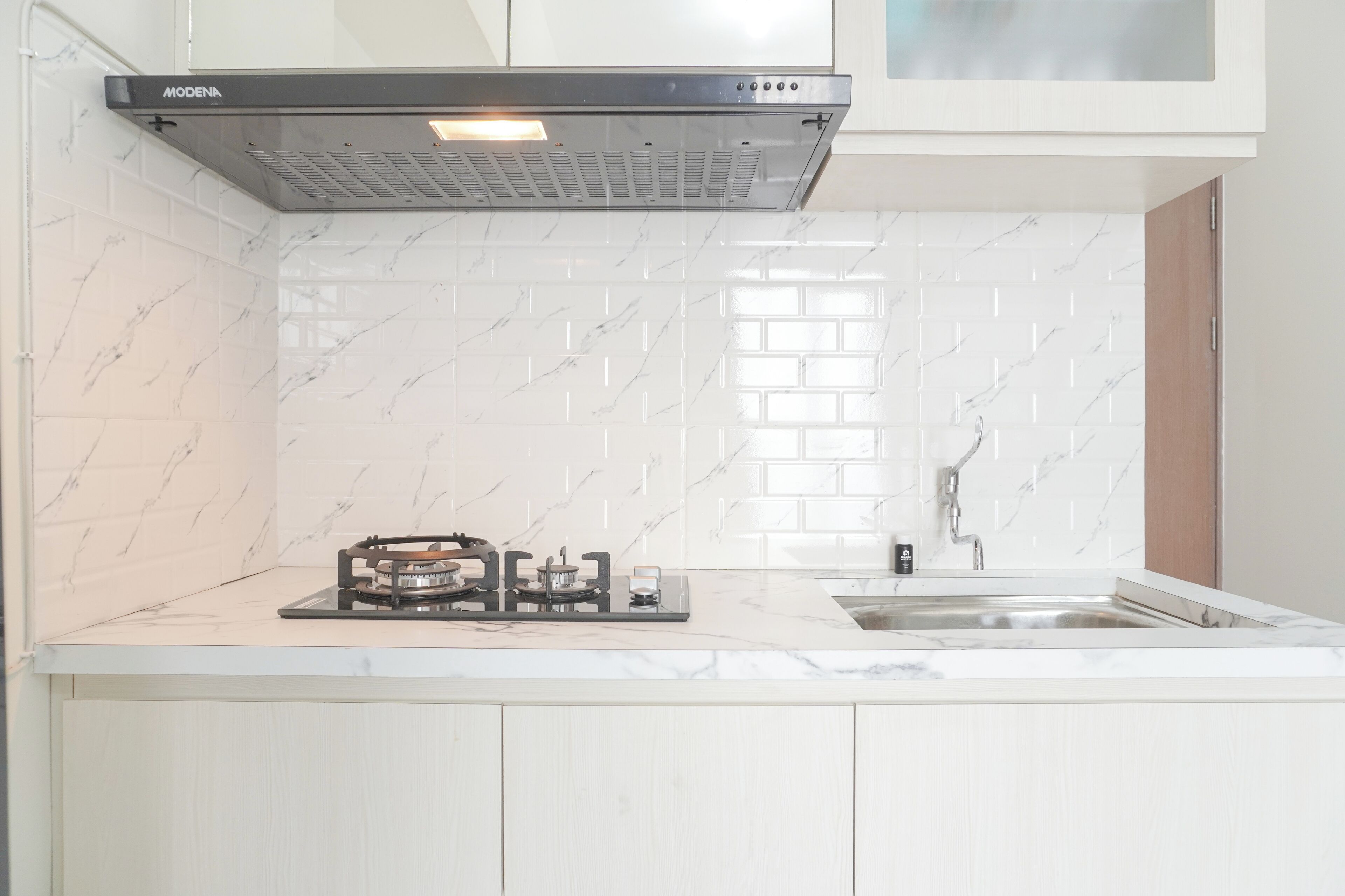 Een moderne keuken met witte marmeren tegels, een gasfornuis en een roestvrijstalen spoelbak.