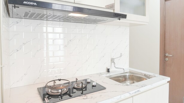 A kitchen with white marble tiles, a gas stove, a stainless steel sink, and a wooden door. - Comfy Stay 2BR at Podomoro Golf View Apartment (Gunung Putri)