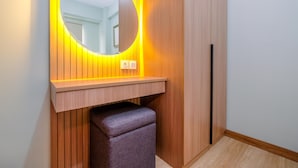A bathroom with a wooden vanity, a round mirror with a yellow backlight, and a small bench. - Nice and Homey 2BR at Podomoro Golf View Apartment (Gunung Putri)