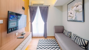 A modern living room with a flat-screen TV, a sofa, a rug, and a painting on the wall. - Nice and Homey 2BR at Podomoro Golf View Apartment (Gunung Putri)