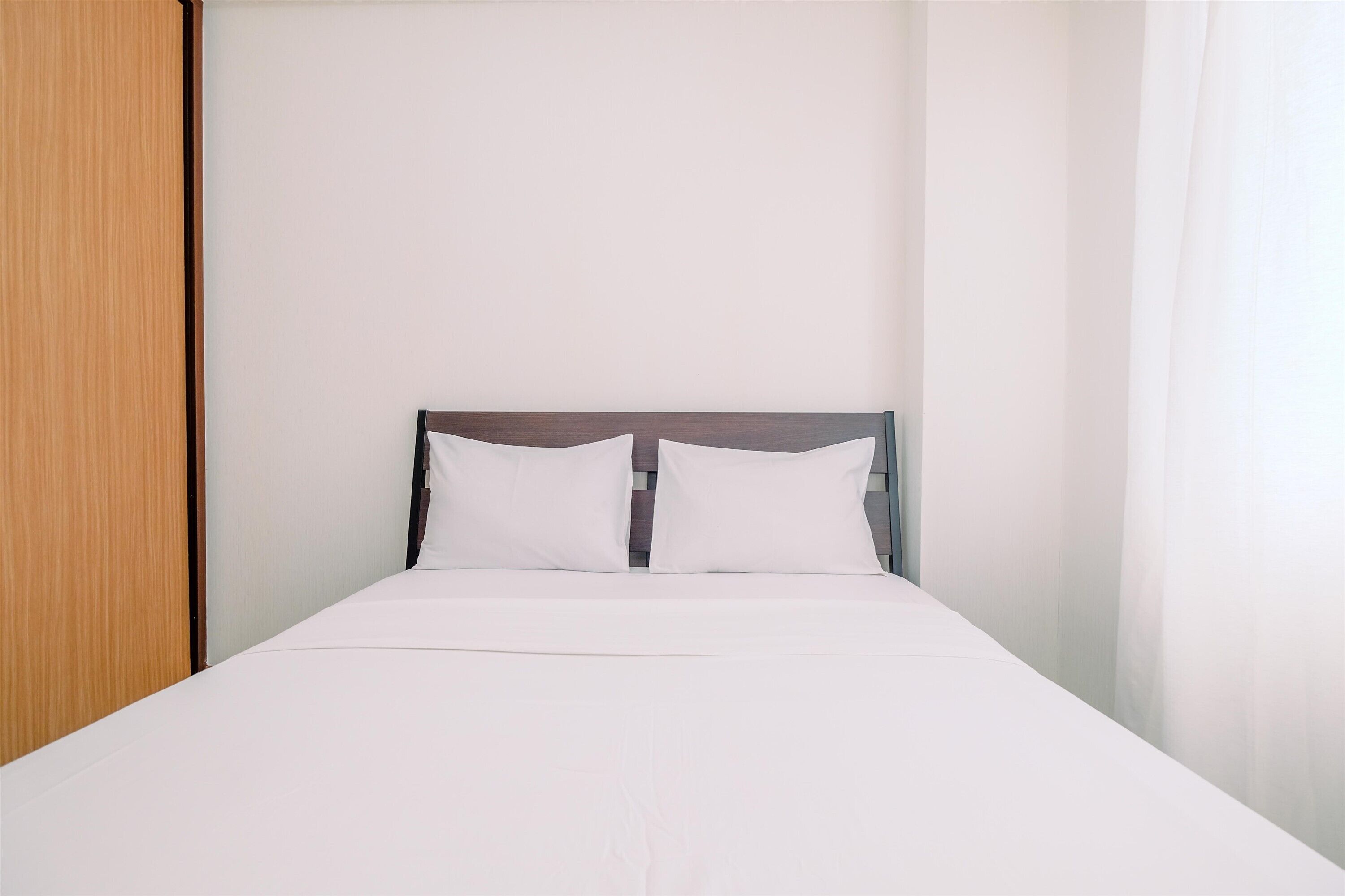 A neatly made bed with white linens and a wooden headboard in a room with plain white walls.