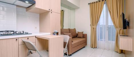 Un espacio habitable compacto con kitchenette, sofá, zona de comedor y televisor montado en la pared.