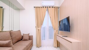Un salon moderne avec un canapé beige, un téléviseur fixé au mur et une porte-fenêtre coulissante avec des rideaux beiges.