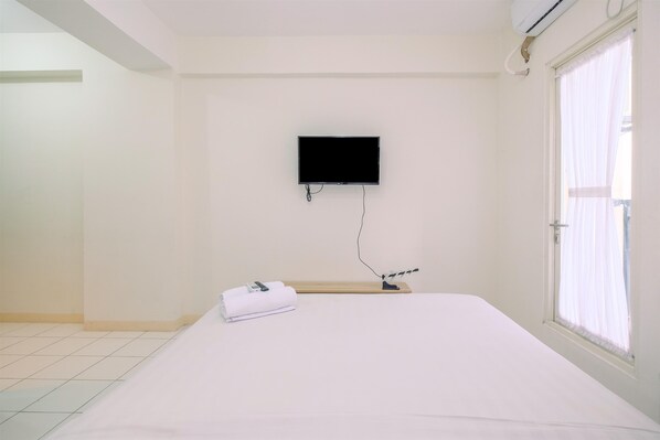 A hotel room with a bed, a flat-screen TV mounted on the wall, a window with curtains, and a towel on the bed.