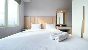A hotel room with a large bed, a wooden headboard, a nightstand, a desk, and a mirror. - Best Deal and Homey 3BR Podomoro Golf View Apartment (Gunung Putri)