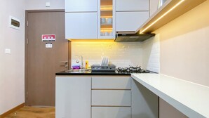A compact kitchen with a gas stove, a sink, and a dish rack. There is a cabinet with a glass door above the sink, and a door with a sign on it. - Best Deal and Homey 3BR Podomoro Golf View Apartment (Gunung Putri)