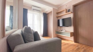A modern living room with a grey sofa, a mounted TV, and wooden shelves. - Best Deal and Homey 3BR Podomoro Golf View Apartment (Gunung Putri)