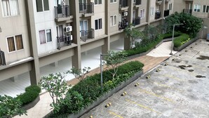 A multi-story residential building with balconies, air conditioning units, and a parking area with bollards.