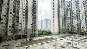 A high-rise residential building with multiple balconies, a parking area, and construction cranes in the background.