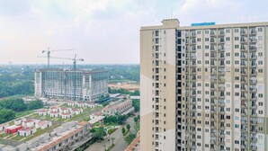 A high-rise building with multiple floors and balconies, surrounded by other buildings and greenery.