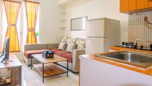 A compact living space with a kitchenette, a sofa, a coffee table, and a flat-screen TV.