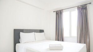 A neatly made bed in a hotel room with a grey headboard, white bedding, and a window with curtains. - Best Choice and Homey 2BR Podomoro Golf View Apartment (Gunung Putri)