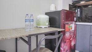 A kitchen with a wooden table, two water bottles, a white coffee maker, a red refrigerator, and a microwave. - Best Choice and Homey 2BR Podomoro Golf View Apartment (Gunung Putri)