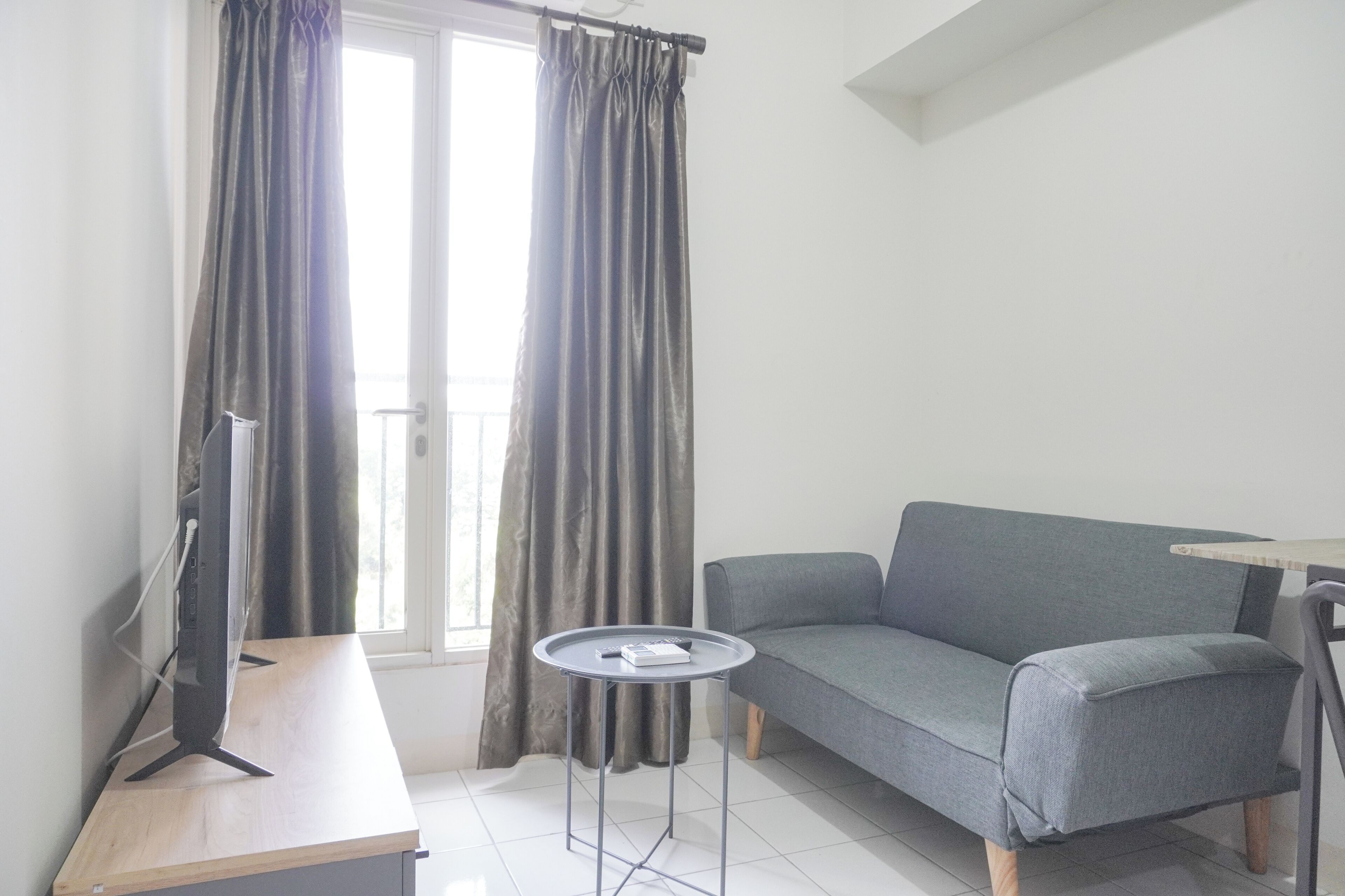 Een moderne woonkamer met een grijze bank, een klein rond tafeltje en een televisie op een houten dressoir.